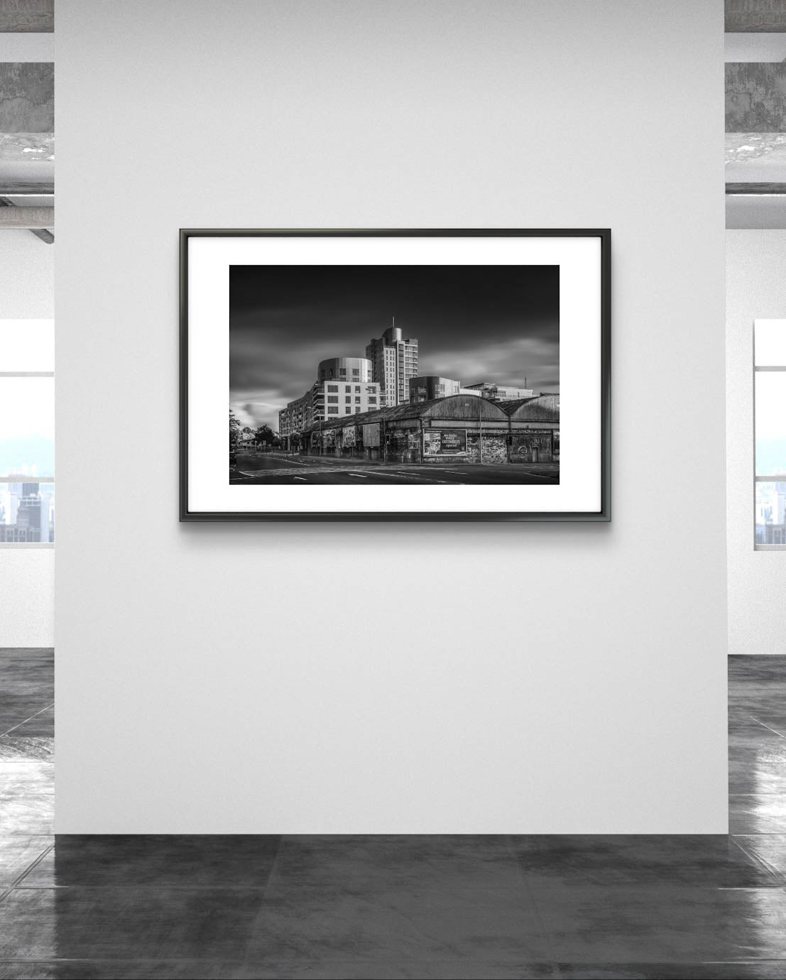 white Wall, framed Black and white photograph of an urban street corner with a row of old, weathered warehouses in the foreground. The warehouses are covered with vintage posters and graffiti. In the background, modern high-rise buildings stand against a dramatic, cloudy sky, contrasting the historic architecture in the foreground. The photo has a moody, timeless atmosphere. Cork City, Ireland. Fine Art Photography. Limited Edition.