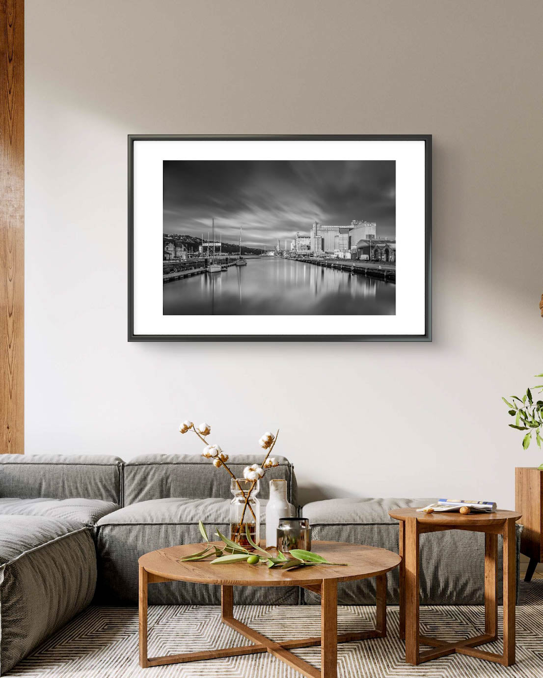 Modern room settings. Black and white framed photograph of a calm waterfront scene with industrial buildings along the right side and several moored boats on the left. The long exposure effect creates smooth water reflections and soft, streaked clouds in the sky, enhancing the tranquil, moody atmosphere of the port area. RH Hall, Port of Cork, Ireland. Fine Art. Limited Edition