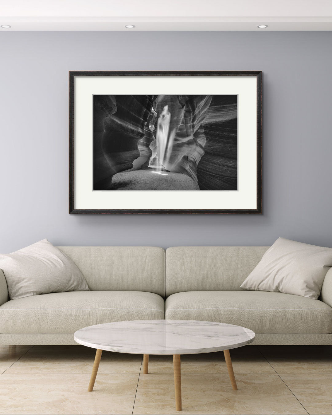 a Modern living rom with huge sofa and coffee table. On the wall is on the wall is hung up black and white photograph of a canyon passage with sand threw in the air in a shape of a ghost. Antelope Canyon. Navajo. Page. Arizona