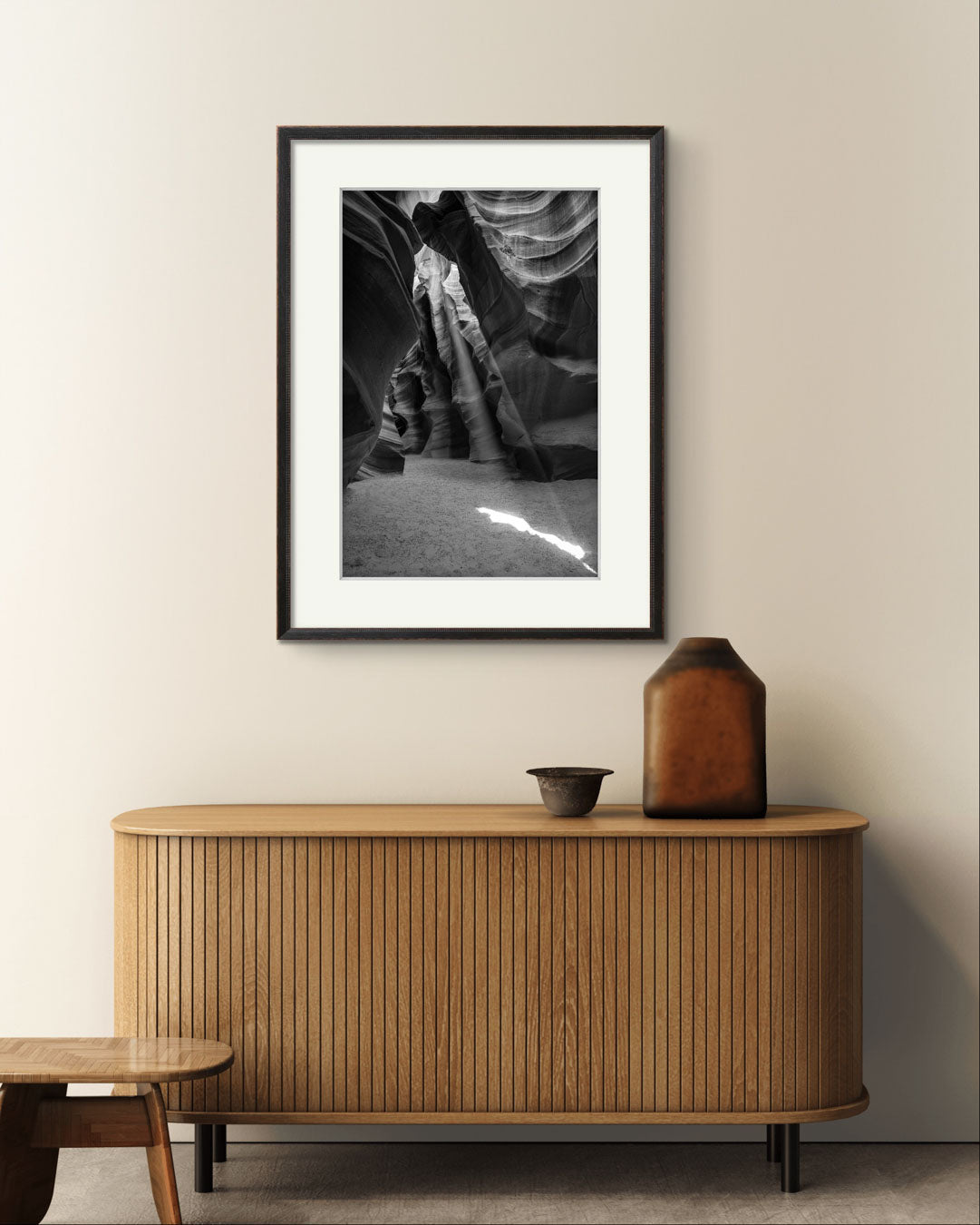 Console wooden table with vase on top and over it is Framed Fine Art black and white photograph of Canyon’s narrow passageway with the light cascading down the walls like a waterfall of illumination. The intricate patterns of the sandstone, carved by centuries of wind and water, create a mesmerizing texture that draws the eye upward. Antelope Canyon, USA, Arizona