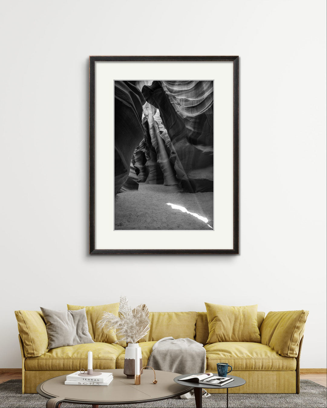 living room settings, yellow puffy sofa with throw and cushions and over it is Framed Fine Art black and white photograph of Canyon’s narrow passageway with the light cascading down the walls like a waterfall of illumination. The intricate patterns of the sandstone, carved by centuries of wind and water, create a mesmerizing texture that draws the eye upward. Antelope Canyon, USA, Arizona