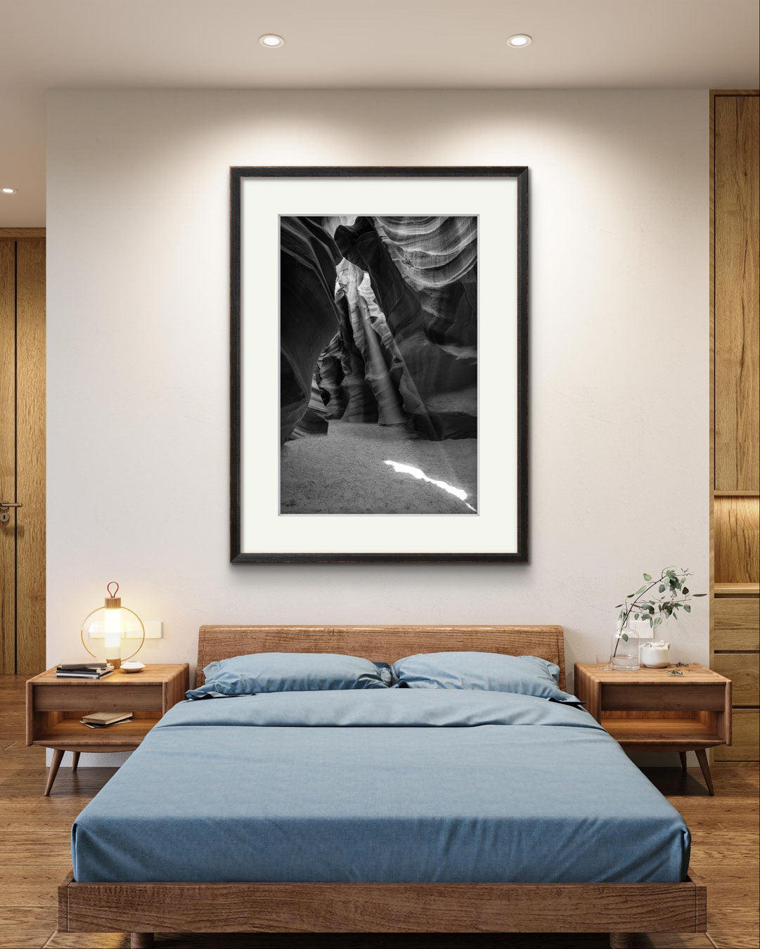 Hotel room wit large bed and 2 side tables and over it is Framed Fine Art black and white photograph of Canyon’s narrow passageway with the light cascading down the walls like a waterfall of illumination. The intricate patterns of the sandstone, carved by centuries of wind and water, create a mesmerizing texture that draws the eye upward. Antelope Canyon, USA, Arizona