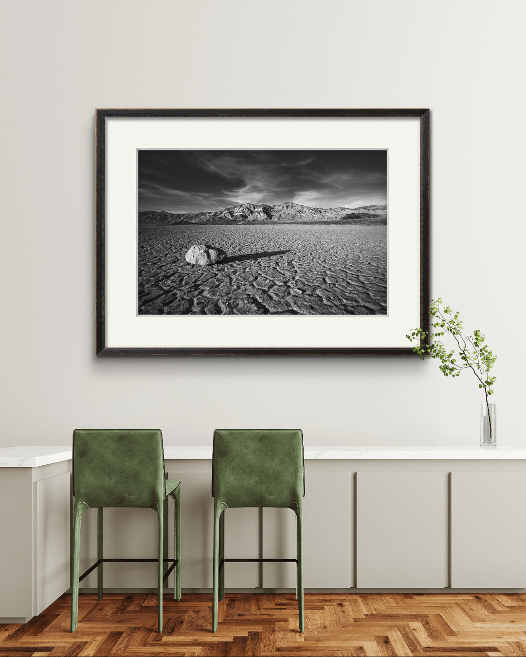 a room with large wall art piece. A desert valley in Eastern California. Black and white fine art framed photograph print of a striking desert landscape in Death Valley National Park. Featuring a solitary rock on the cracked, dry lakebed of the Racetrack Playa, mountain ranges in the background. Perfect for home decor, unique nature and landscape prints, the spirit of American Southwest.