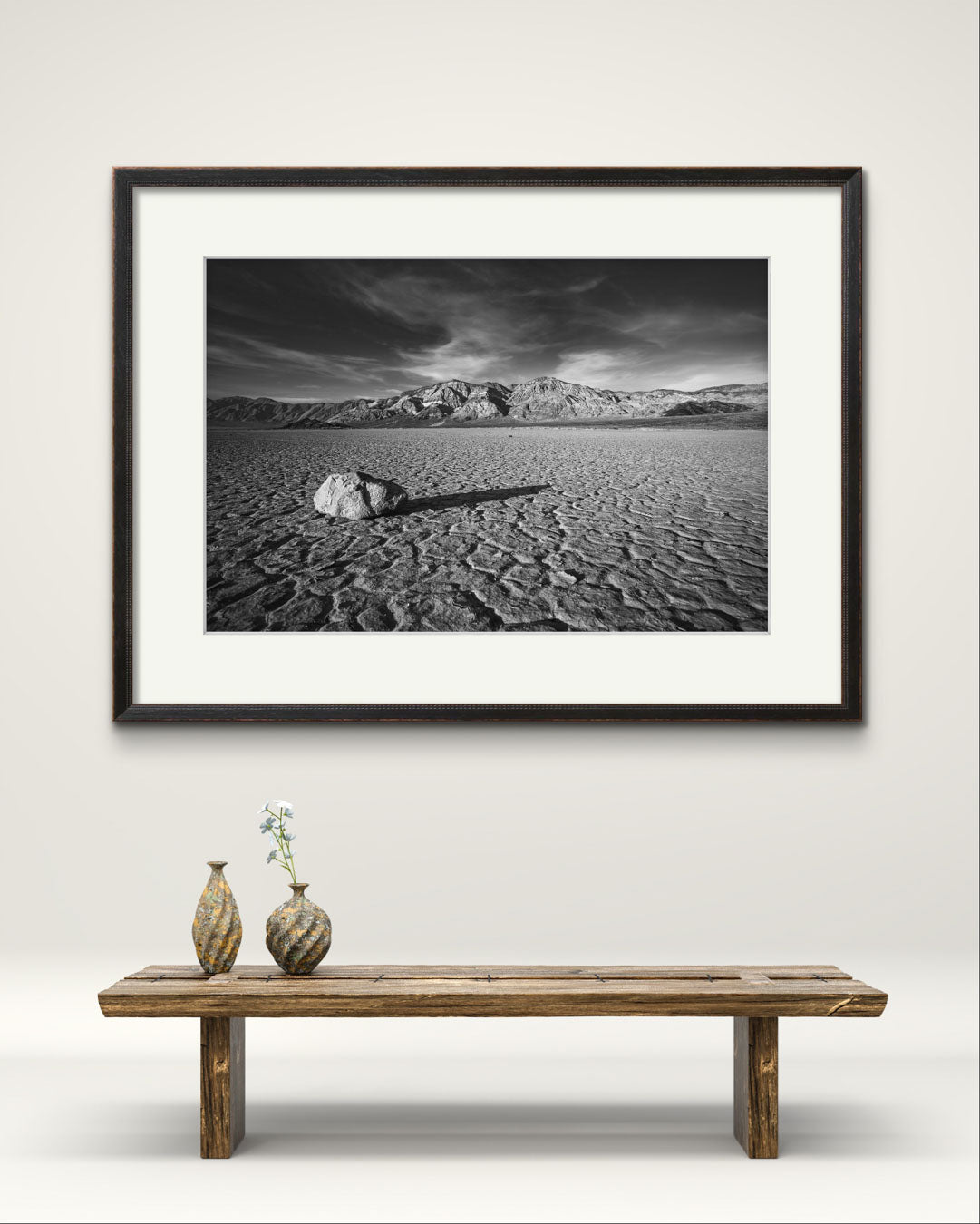 A desert valley in Eastern California. Black and white fine art framed photograph print of a striking desert landscape in Death Valley National Park. Featuring a solitary rock on the cracked, dry lakebed of the Racetrack Playa, mountain ranges in the background. Perfect for home decor, wall art, or photography enthusiasts seeking unique nature and landscape prints, this image captures the stark beauty, texture, and timeless appeal of the American Southwest.