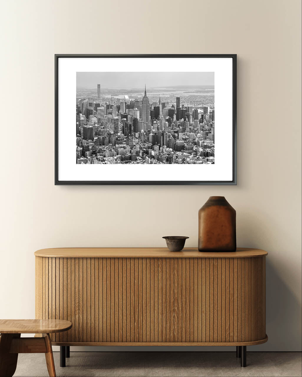 wooden console table with vases on top. greyish wall and framed black and white fine art photography print. Aerial view of Manhattan with the iconic Empire State Building reigning supreme at its center. The photograph captures the city in all its grandeur, with skyscrapers reaching for the sky and the bustling streets below. NYC. New York City