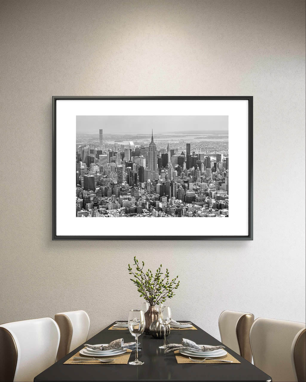 Dining table with plates and decoration on it. on the wall in the background framed black and white fine art photography print. Aerial view of Manhattan with the iconic Empire State Building reigning supreme at its center. The photograph captures the city in all its grandeur, with skyscrapers reaching for the sky and the bustling streets below. NYC. New York City