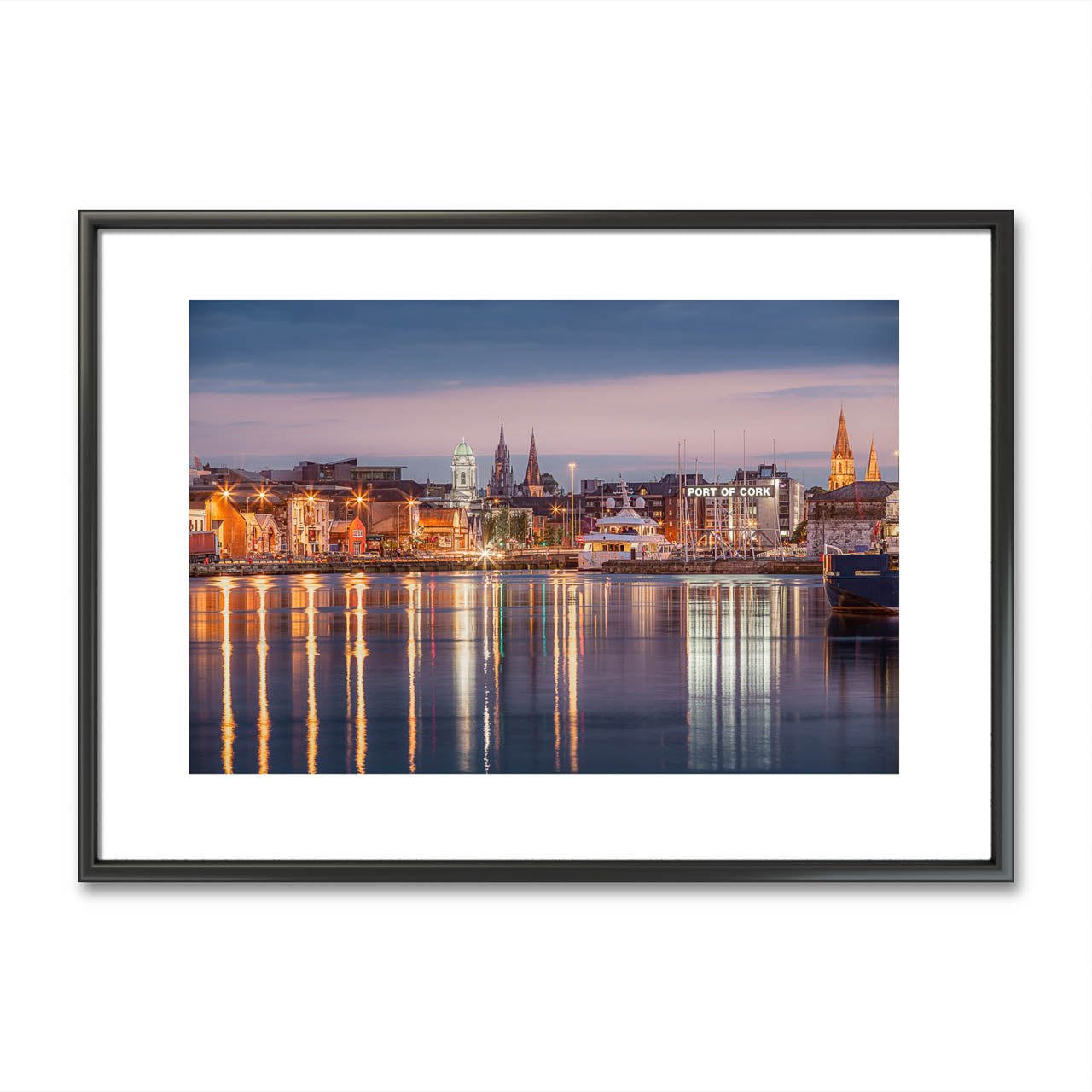 Framed colour fine art photograph print  of Cork City, Ireland, displayed on a minimalist wall. The photo captures a serene waterfront view with reflections of historic buildings and church spires in the water. Limited Edition