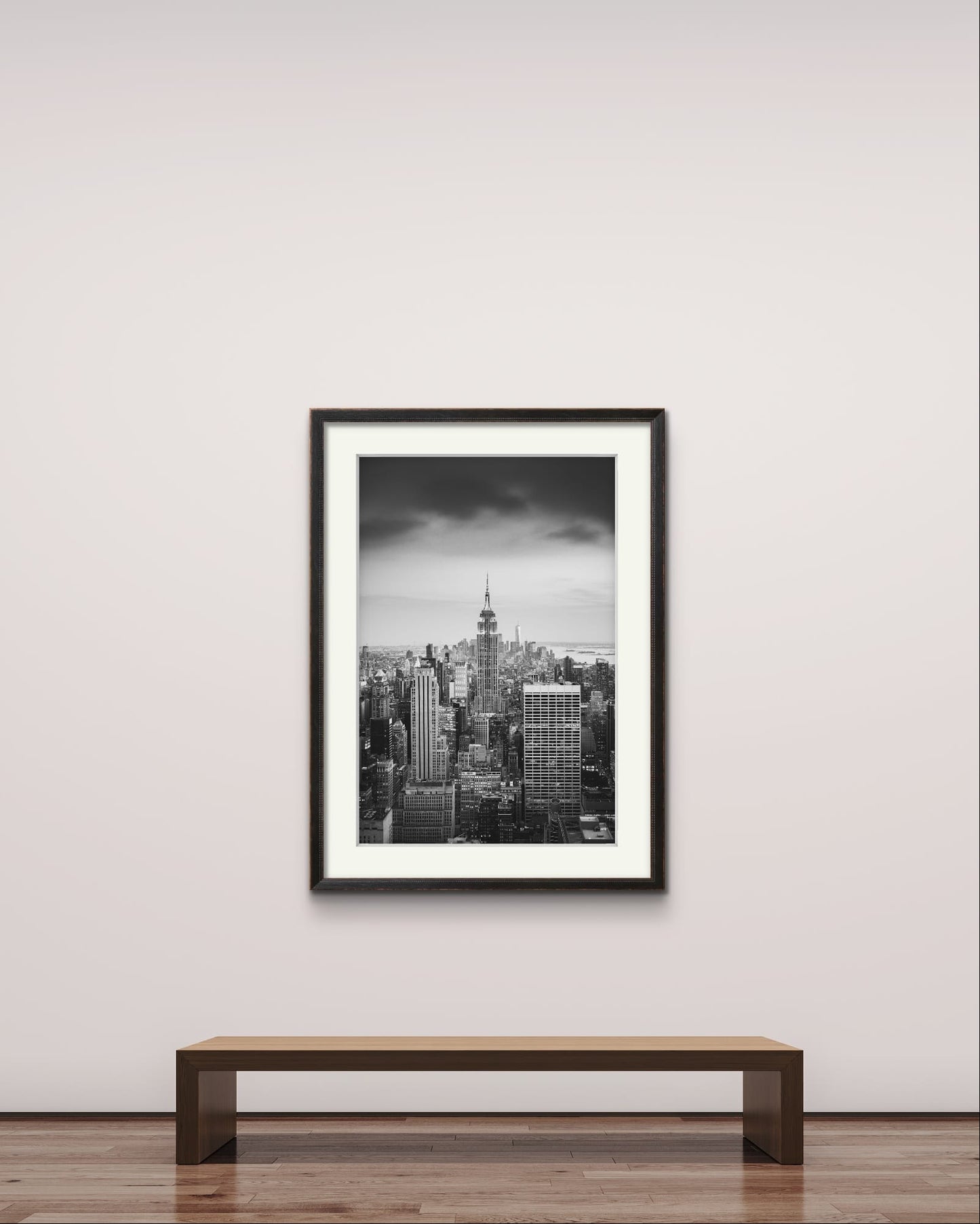 Like a museum setting. just a bench in front of Black and white photography print. A breathtaking view of Manhattan from the terrace of the Rockefeller Centre, looking southward, with the majestic Empire State Building commanding the scene as the focal point. New York City.
