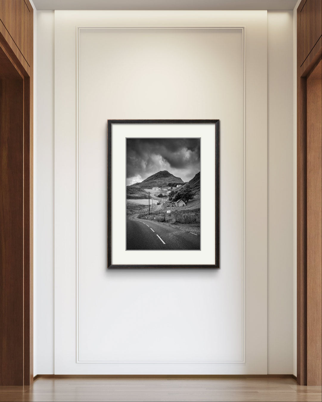 A hall wall. on the wall Framed black and white fine art photography print showcasing Irish landscape. The twisting road and houses create a magical scenery of rural Ireland. Co. Donegal. Teelin