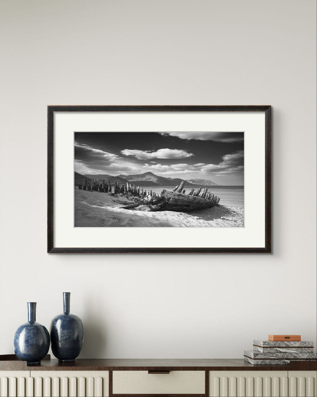 A long console table with two navy vases and above is hung framed photography print of Irish coastal landscape. The wreck of ship in a focal point. behind hills and ocean. Wild Atlantic Way. Rossbeigh Beach. Kerry. Ireland.