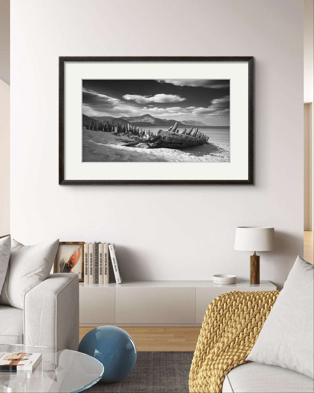 A living room with sofas an by the back wall is hung framed photography print of Irish coastal landscape. The wreck of ship in a focal point. behind hills and ocean. Wild Atlantic Way. Rossbeigh Beach. Kerry. Ireland.