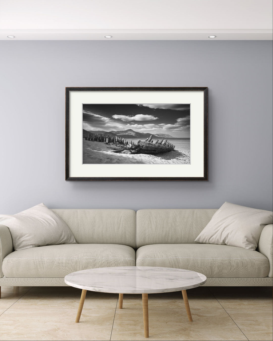 A Large sofa with a coffee table in front. On the wall framed photography print of Irish coastal landscape. The wreck of ship in a focal point. behind hills and ocean. Wild Atlantic Way. Rossbeigh Beach. Kerry. Ireland.