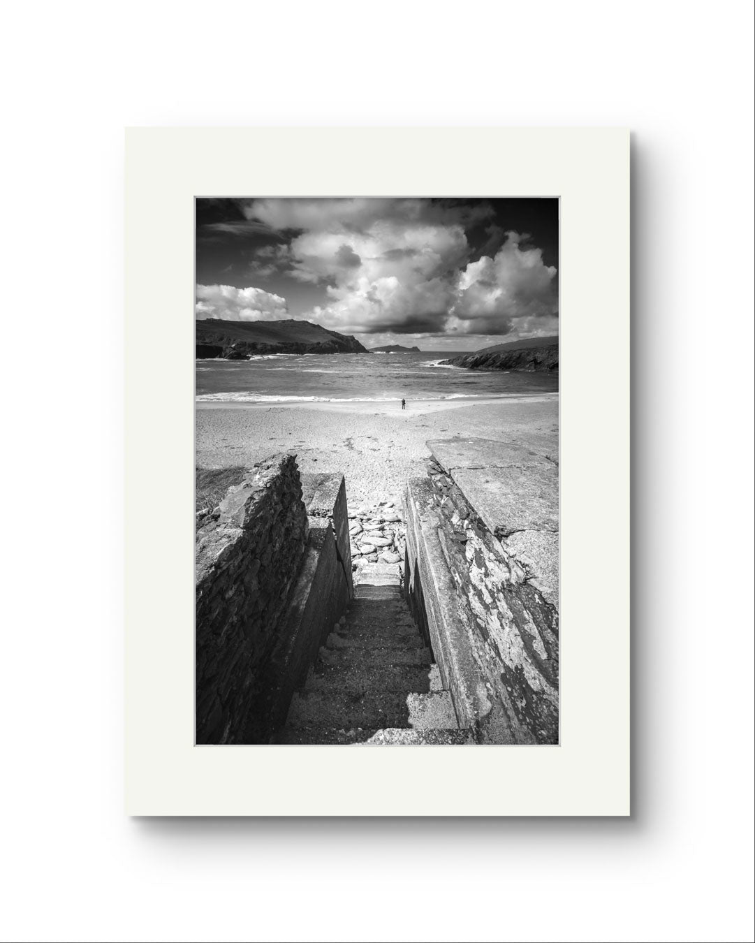 Black and white photograph of an Irish Coast, dynamic composition draws your eyes to an ocean and a person walking on the distance beach. Clogher Beach. Dingle Town. Slea Head Drive in County Kerry.