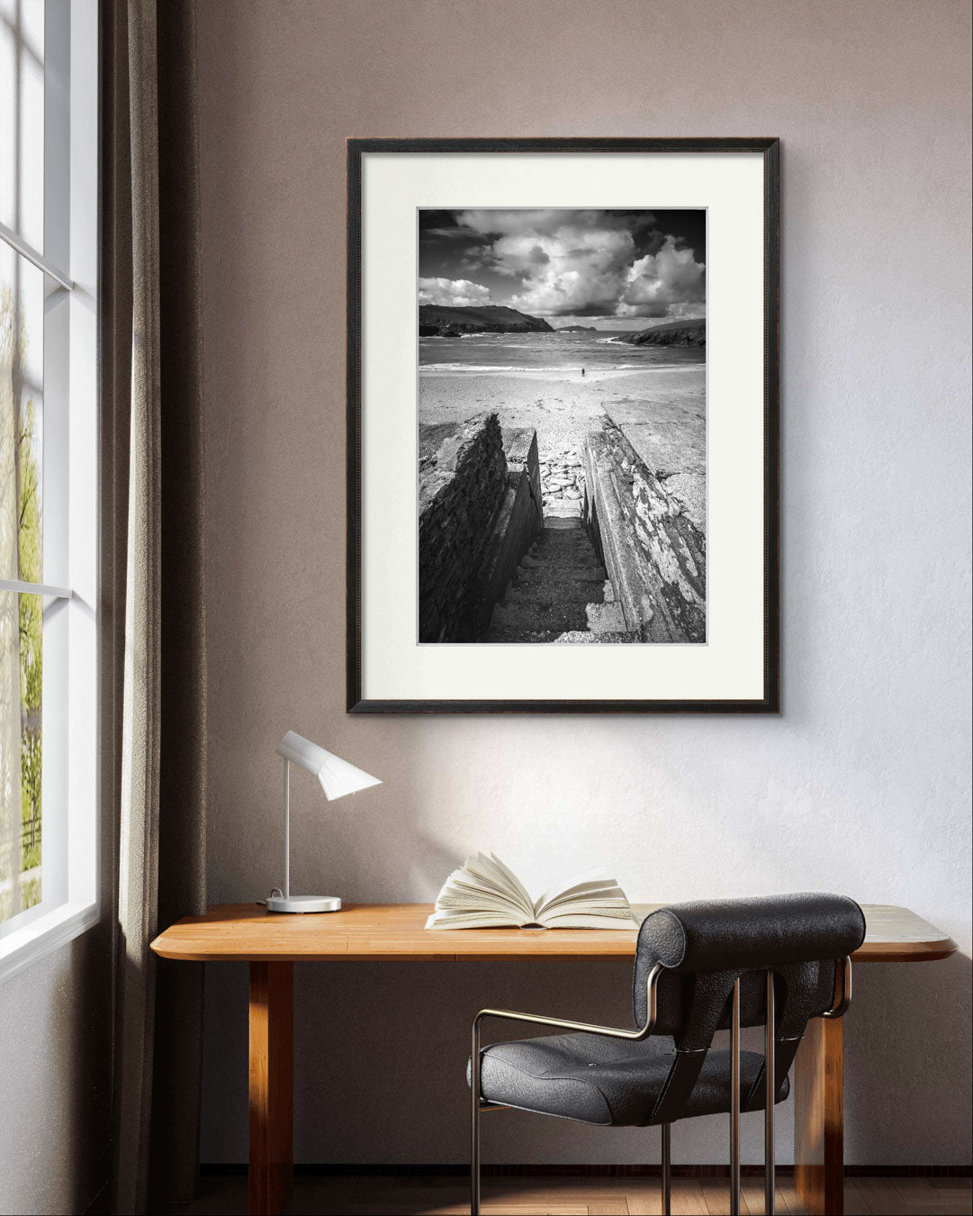 small room with a desk and chair and over it is framed photograph of an Irish Coast, dynamic composition draws your eyes to an ocean and a person walking on the distance beach. Clogher Beach. Dingle Town. Slea Head Drive in County Kerry.