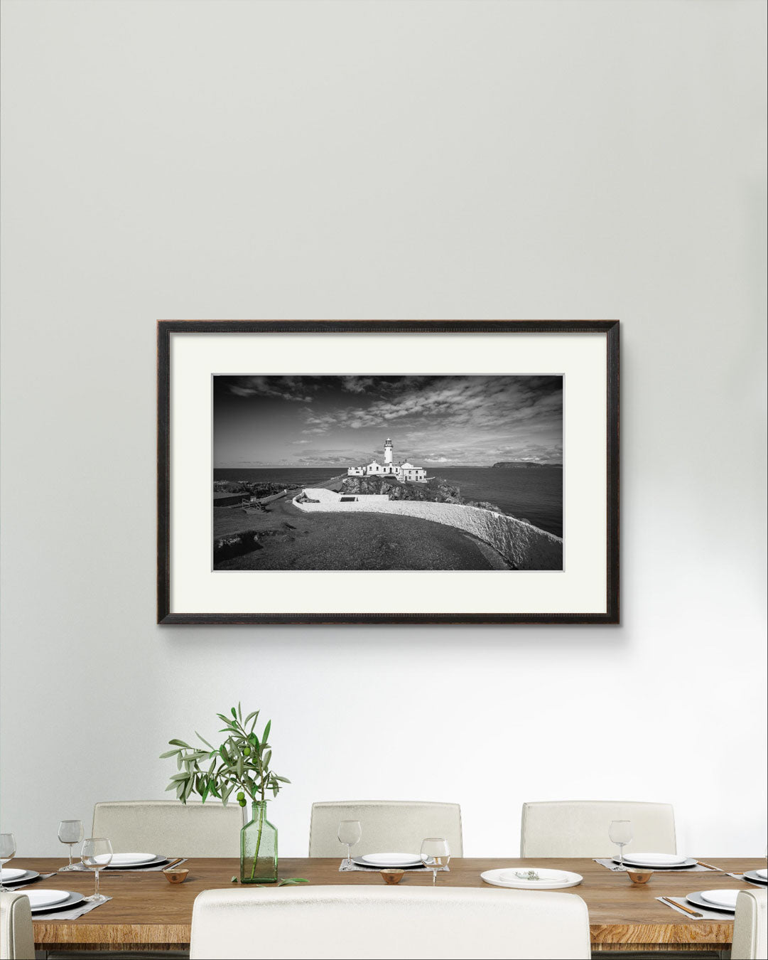 a dining table and a view of a a framed photograph of Irish coastal landscape with a lighthouse in a focal point. Fanad Head. Donegal. Wild Atlantic Way.