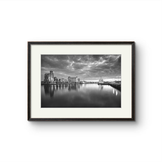 Black and white Fine Art Photography Print. The calm river reflects lights from buildings along the shoreline, creating a shimmering effect on the water. A cloudy sky adding a serene, moody atmosphere. The industrial buildings lights contrast with the darkening sky, giving the scene a peaceful atmosphere. RH Hall, Kennedy Quay, Port of Cork, Limited Edition Print, Cork City, Ireland