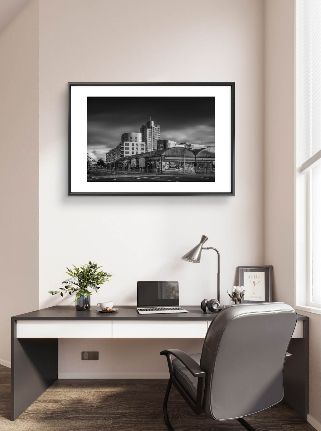 Home office, framed Black and white photograph of an urban street corner with a row of old, weathered warehouses in the foreground. The warehouses are covered with vintage posters and graffiti. In the background, modern high-rise buildings stand against a dramatic, cloudy sky, contrasting the historic architecture in the foreground. The photo has a moody, timeless atmosphere. Cork City, Ireland. Fine Art Photography. Limited Edition.