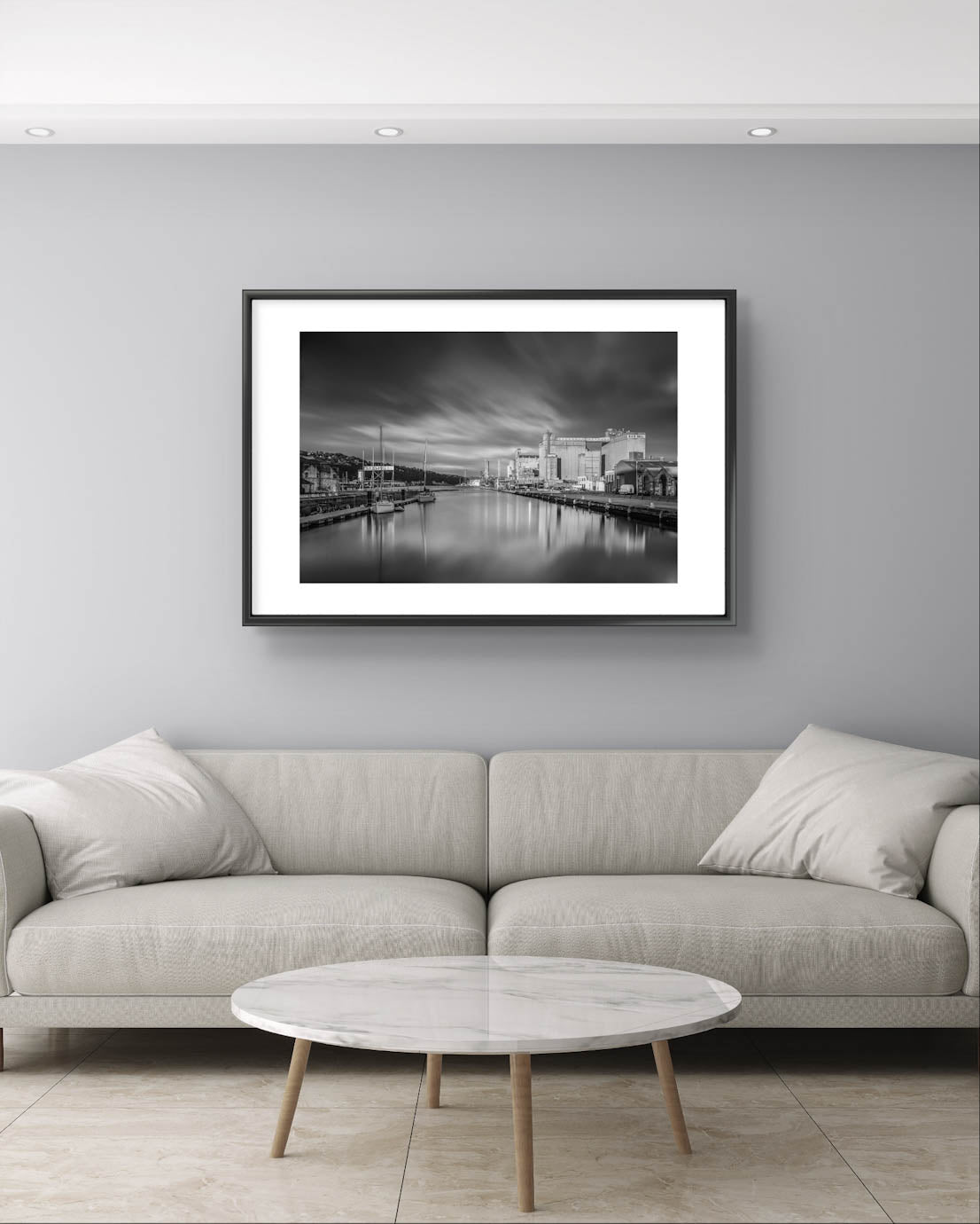 Large sofa and Black and white framed photograph hanging on the wall. A calm waterfront scene with industrial buildings along the right side and several moored boats on the left. The long exposure effect creates smooth water reflections and soft, streaked clouds in the sky, enhancing the tranquil, moody atmosphere of the port area. RH Hall, Port of Cork, Ireland. Fine Art. Limited Edition