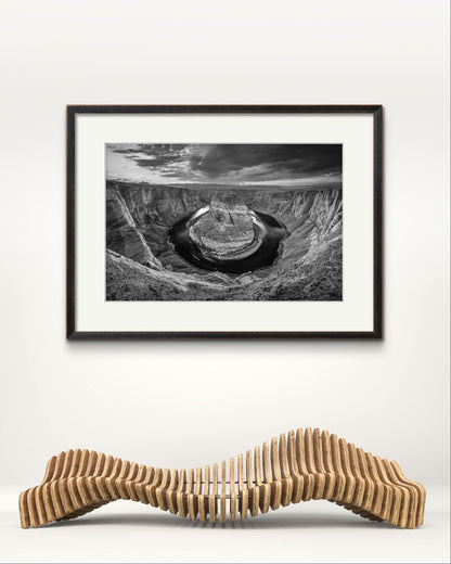 musem room with a  wavy bench. On the Wall is  a large wall art. Black and white fine art photography print of a horseshoe-shaped incised meander of the Colorado River, Page, Arizona. USA