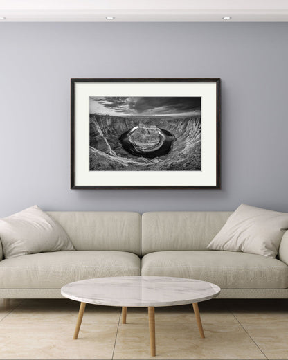 A nice comfy bright sofa. Above is modern home decor piece. wall art. Black and white fine art photography print of a horseshoe-shaped incised meander of the Colorado River, Page, Arizona. USA