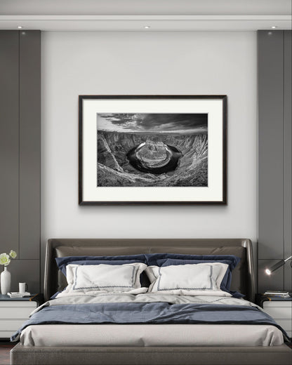 a hotel room with large bed. Above is hanging large wall art. Black and white fine art photography print of a horseshoe-shaped incised meander of the Colorado River, Page, Arizona. USA