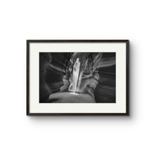 black and white photography of a canyon passage with sand threw in the air  in a shape of a ghost. Antelope Canyon. Navajo. Page. Arizona