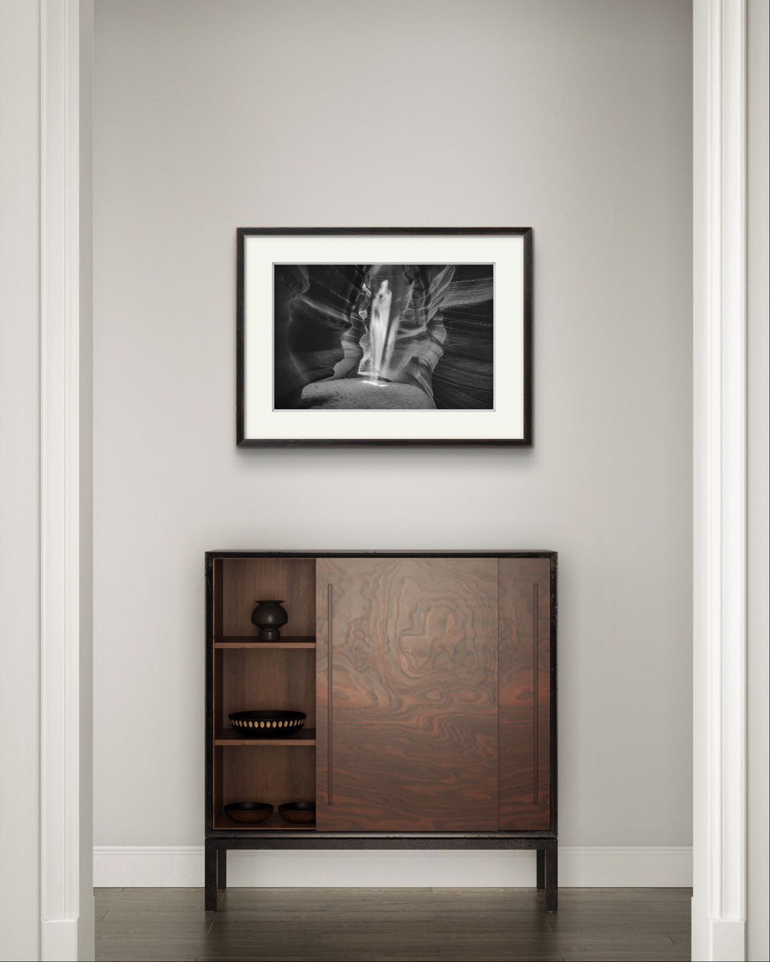 A hall at modern home. on the greyish wall just above a stylish console table is a black and white photography of a canyon passage with sand threw in the air  in a shape of a ghost. Antelope Canyon. Navajo. Page. Arizona