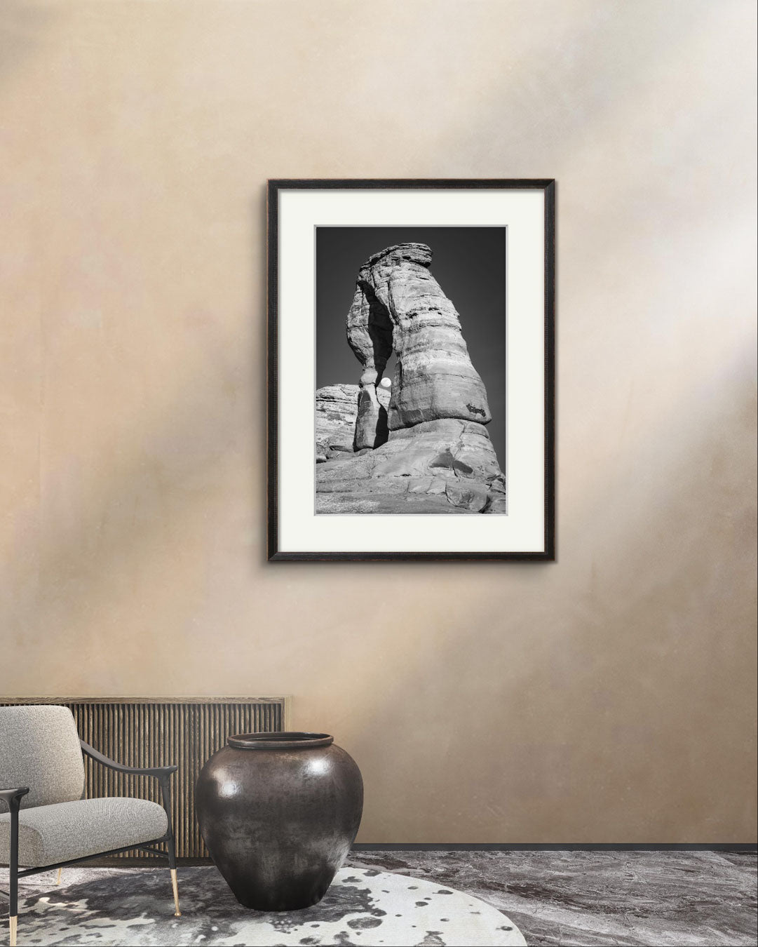 Waiting room in exclusive building, a chair and large vase on the floor. Room is decorated with Framed Fine Art black and white photograph of impressive large arch and visible moon through it. Delicate Arch, Moab, USA, Arches National Park