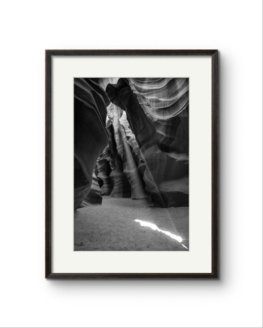 Framed Fine Art black and white photograph of Canyon’s narrow passageway with the light cascading down the walls like a waterfall of illumination. The intricate
patterns of the sandstone, carved by centuries of wind and water, create a mesmerizing texture that draws the eye upward. Antelope Canyon, USA, Arizona