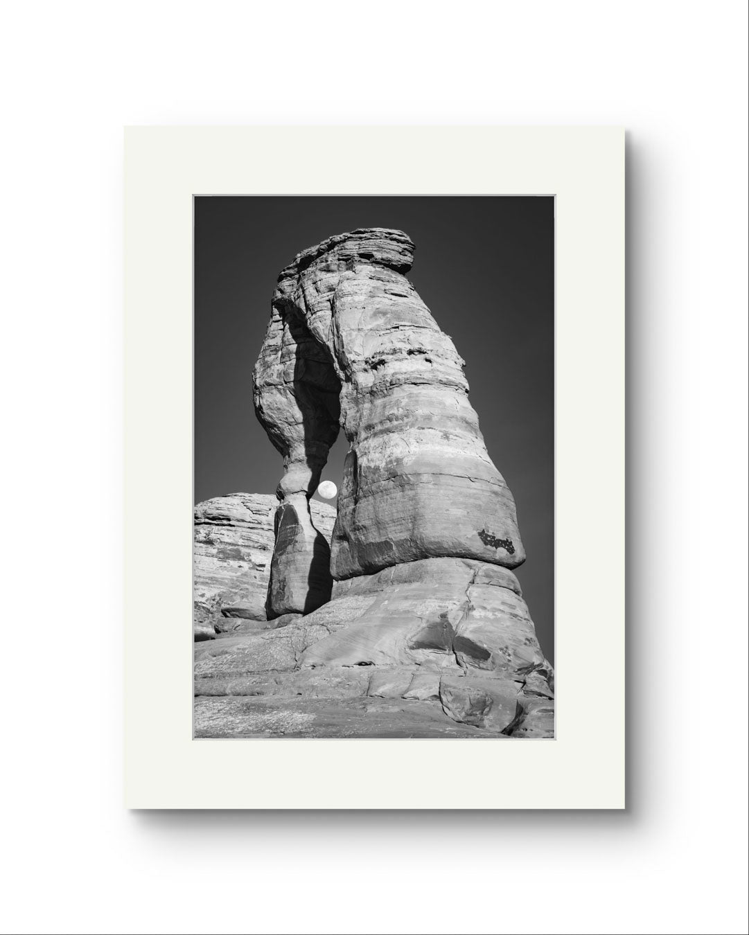 Unframed Fine Art black and white photograph of impressive large arch 
 and visible moon through it. Delicate Arch, Moab, USA, Arches National Park