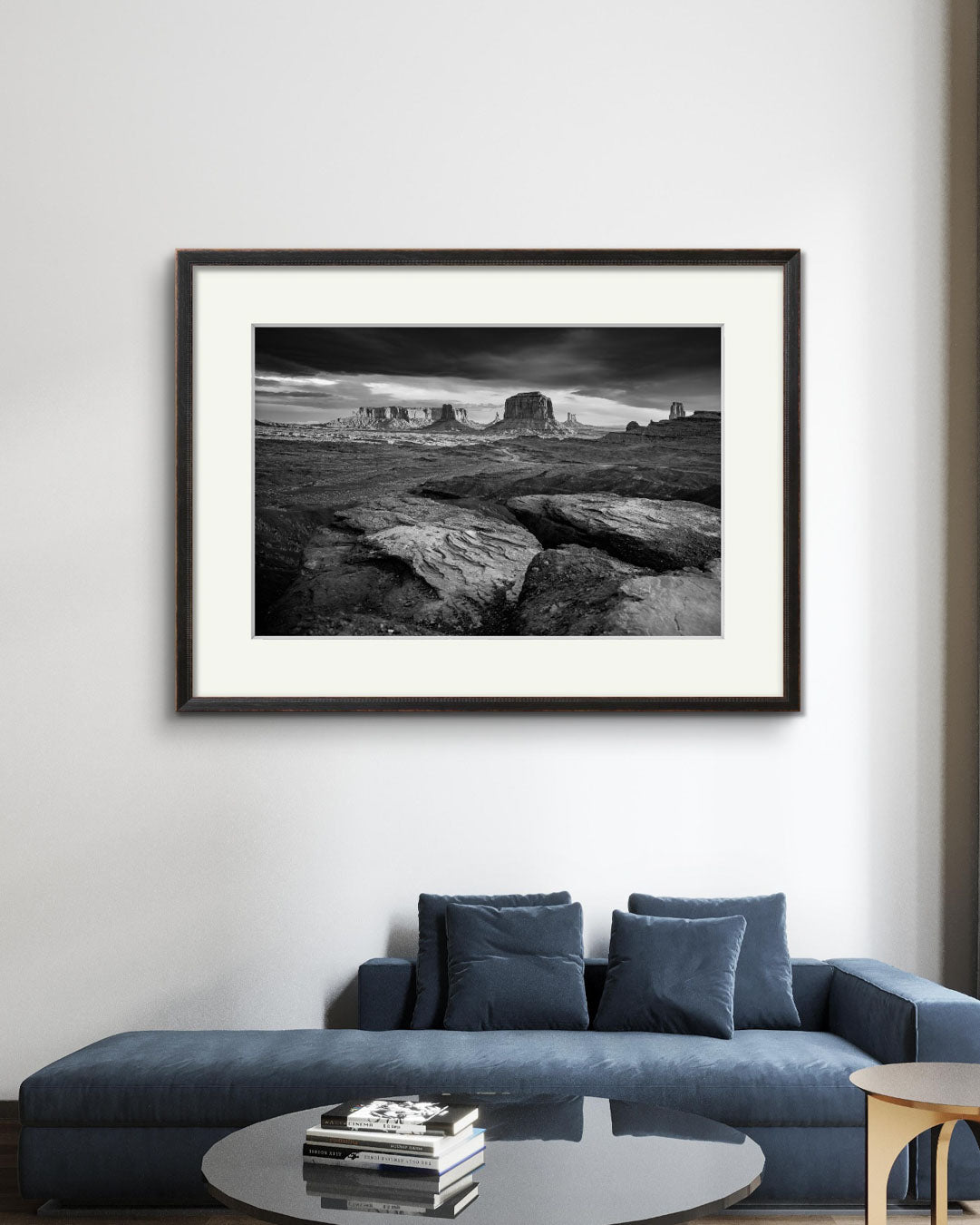 A Navy sofa. above is large piece of modern home decor wall art. Framed fine art photography print showcasing one of the most iconic and scenic spots in the Navajo Tribal Park in Monument Valley. Lookout with sweeping vistas of craggy buttes. USA