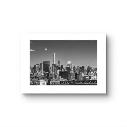 Unframed black and white photograph of New York City skyline. All buildings towering behind the waterfront. Taken from Brooklyn Bridge side. Manhattan, NYC, USA