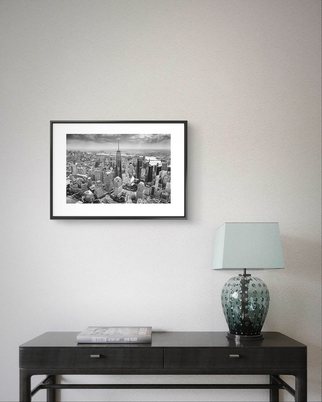 Console table with a lamp on right hand side nd over it hanging Black and white photograph of skyscrapers an buildings of New York City. Helicopter View. Focal point is One World Trade Center. 