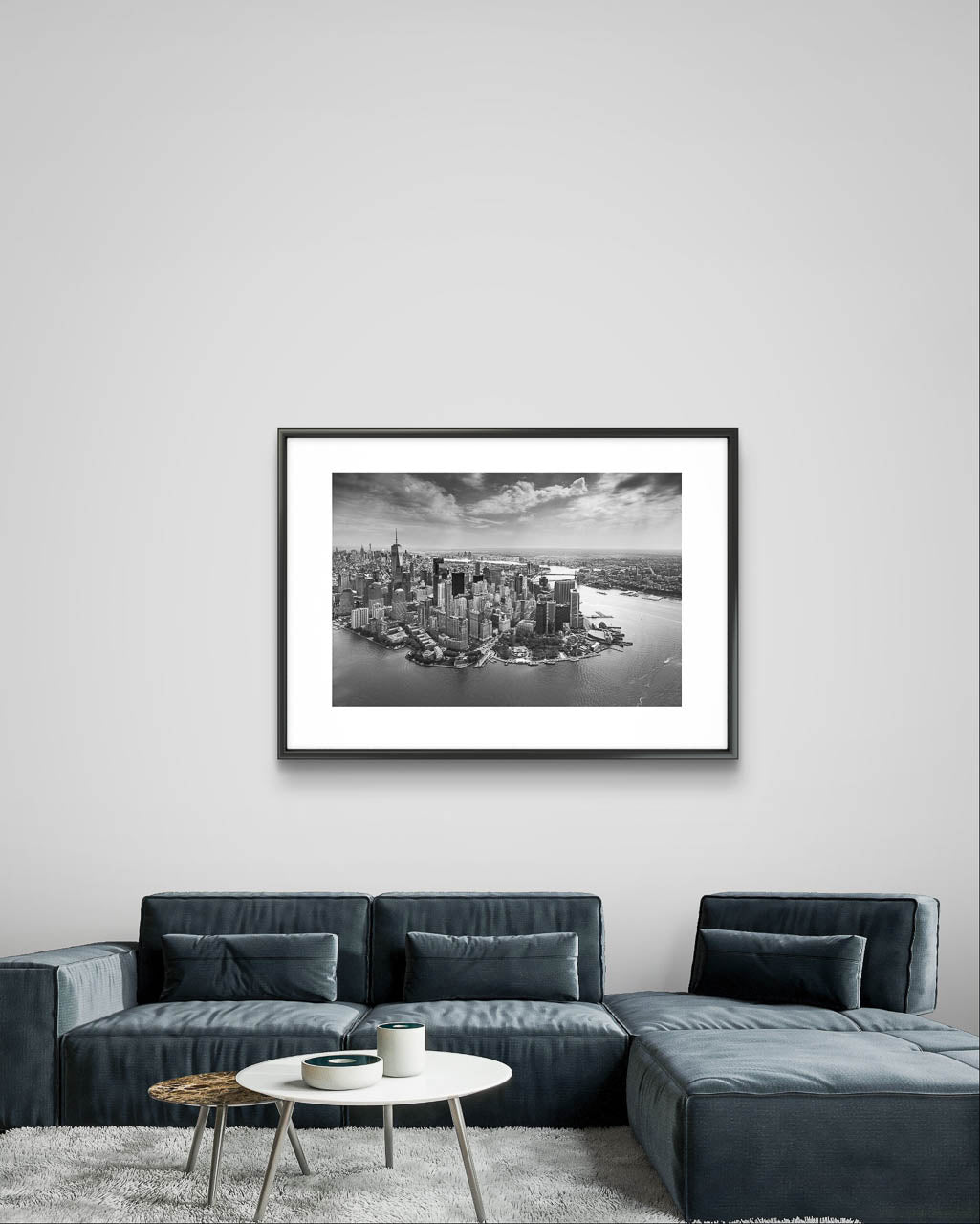 Modern home living room with large, dark sofa and coffee table. On the wall Framed black and white fine art photography Print. Aerial view of Manhattan. Financial District and towering skyscrapers of Wall Street. New York City.