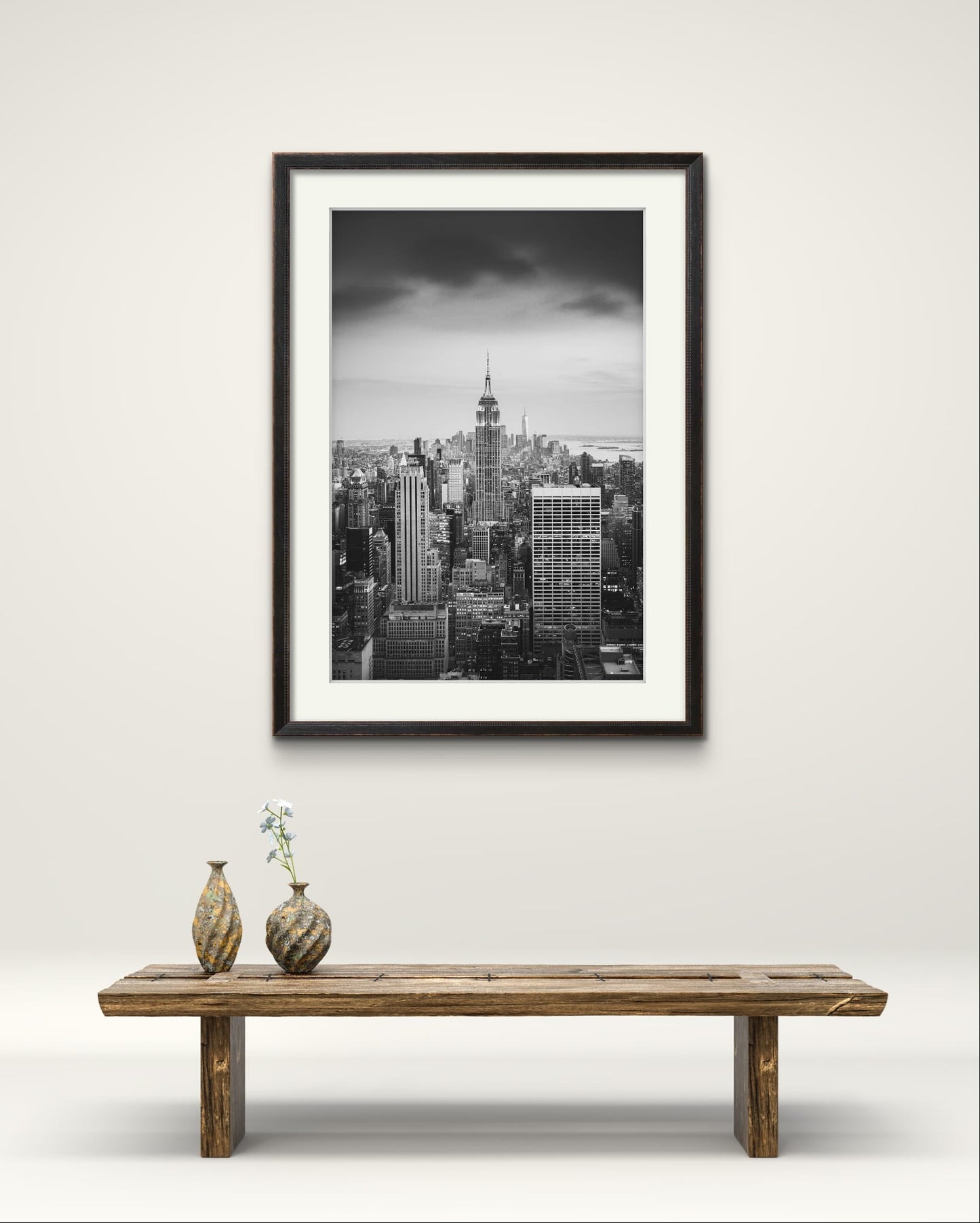 a wooden bench with 2 vases on the left hand side.  in the background is Black and white photography print. A breathtaking view of Manhattan from the terrace of the Rockefeller Centre, looking southward, with the majestic Empire State Building commanding the scene as the focal point. New York City.