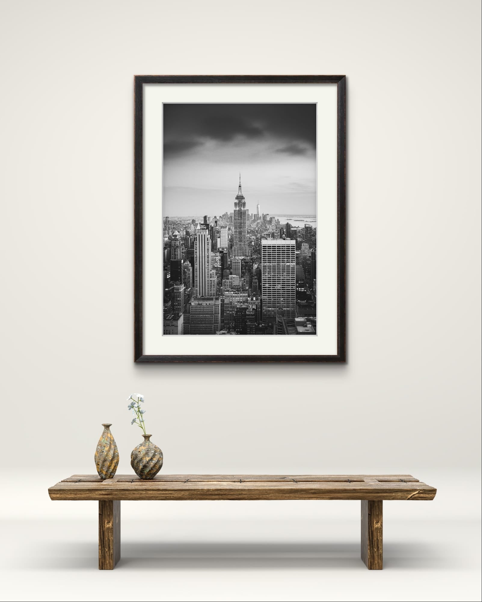 a wooden bench with 2 vases on the left hand side.  in the background is Black and white photography print. A breathtaking view of Manhattan from the terrace of the Rockefeller Centre, looking southward, with the majestic Empire State Building commanding the scene as the focal point. New York City.